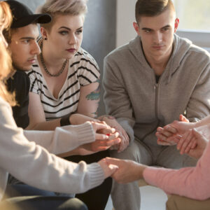 Groupe de jeunes se tenant la main en cerclant avec un psychologue