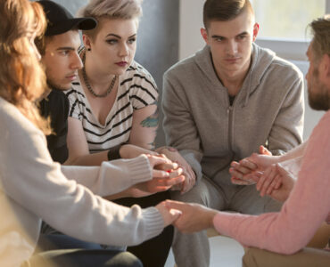 Groupe de jeunes se tenant la main en cerclant avec un psychologue