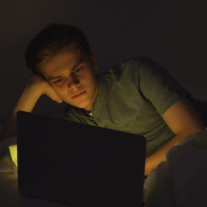 Teenage boy using laptop on bed at night. Internet addiction